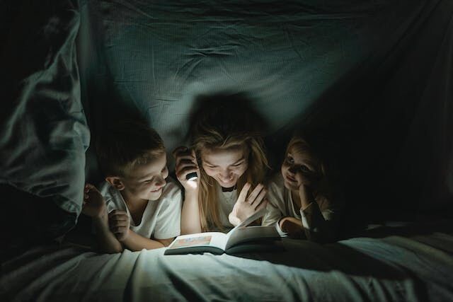 Children read book under covers using small flashlight